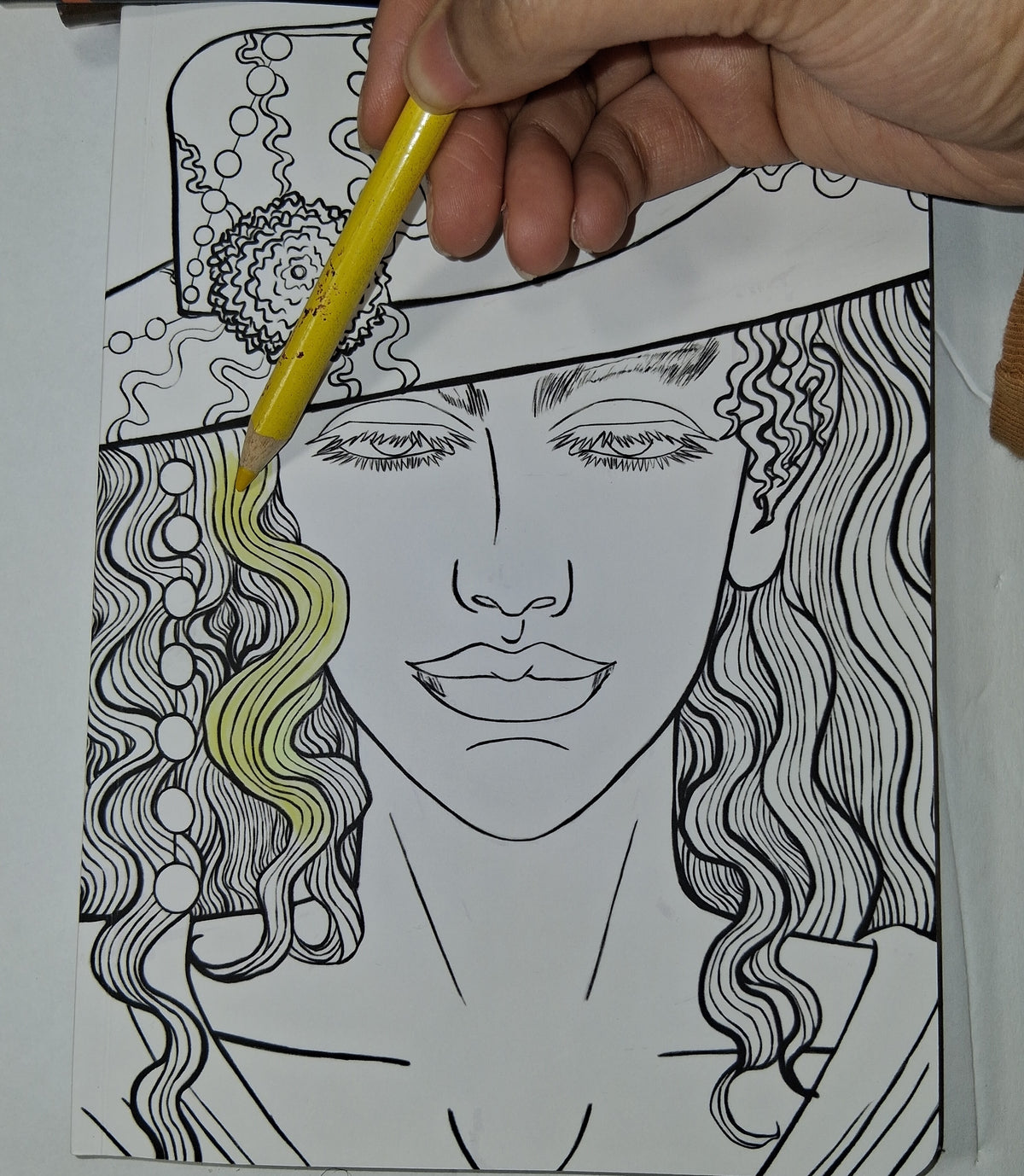 Hand coloring a black and white illustration of a woman's face with a yellow pencil.