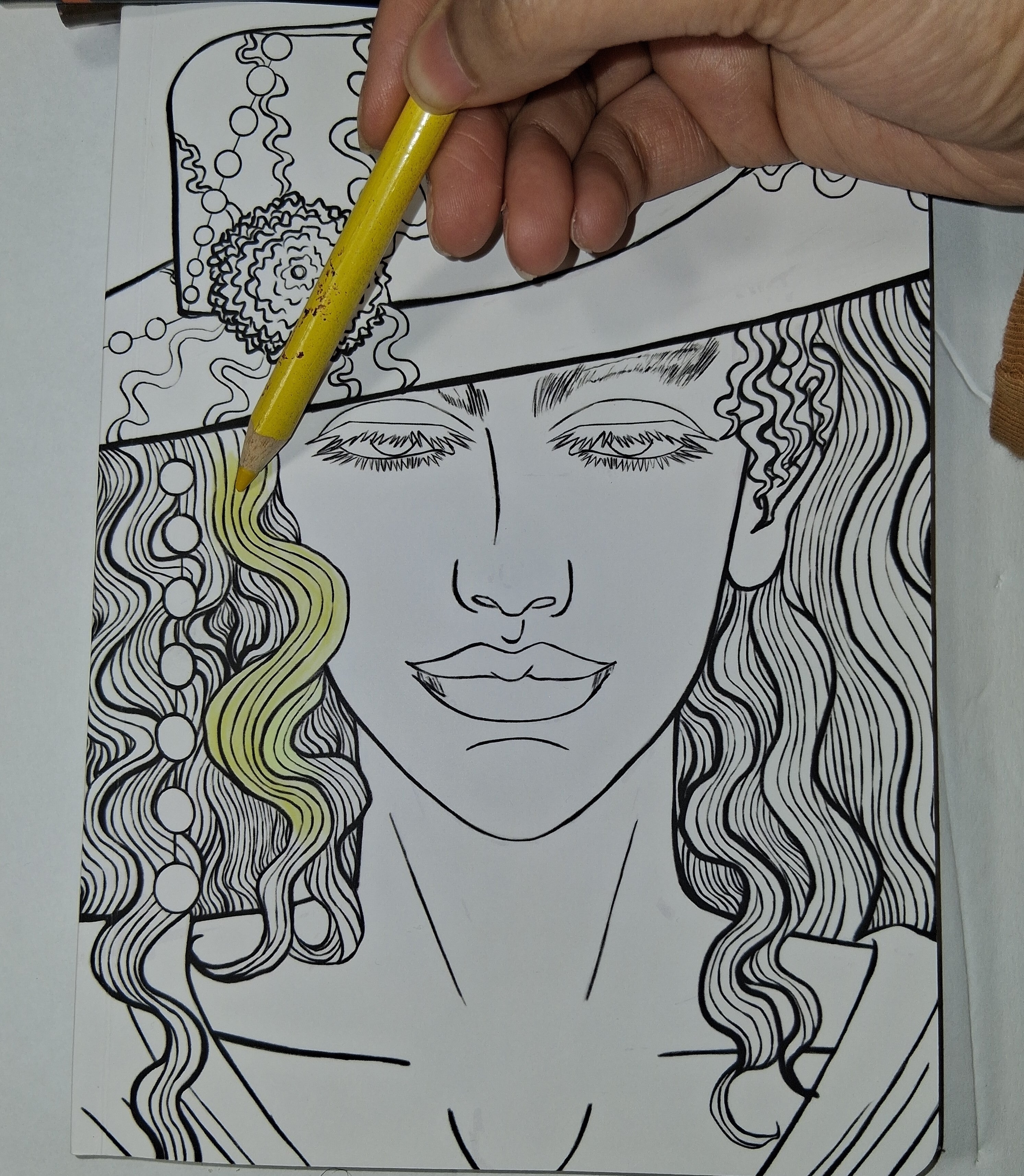 Hand coloring a black and white illustration of a woman's face with a yellow pencil.